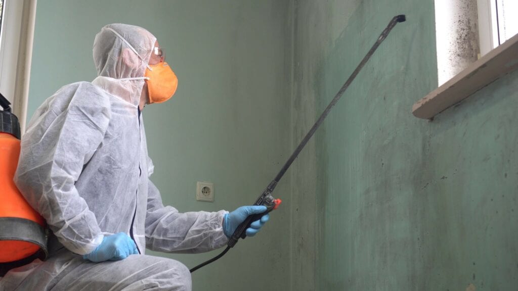 A man in a protective suit, glasses and a respirator sprays a disinfectant