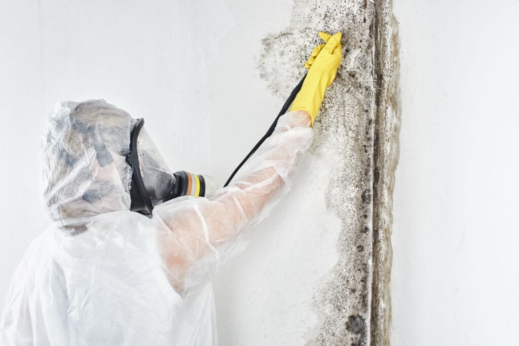 A person in white suit and yellow mask cleaning wall.