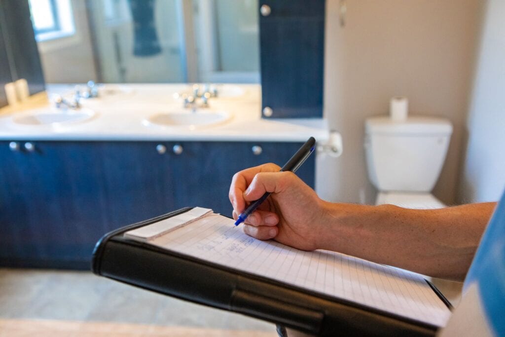 A person writing on paper in front of a bathroom sink.