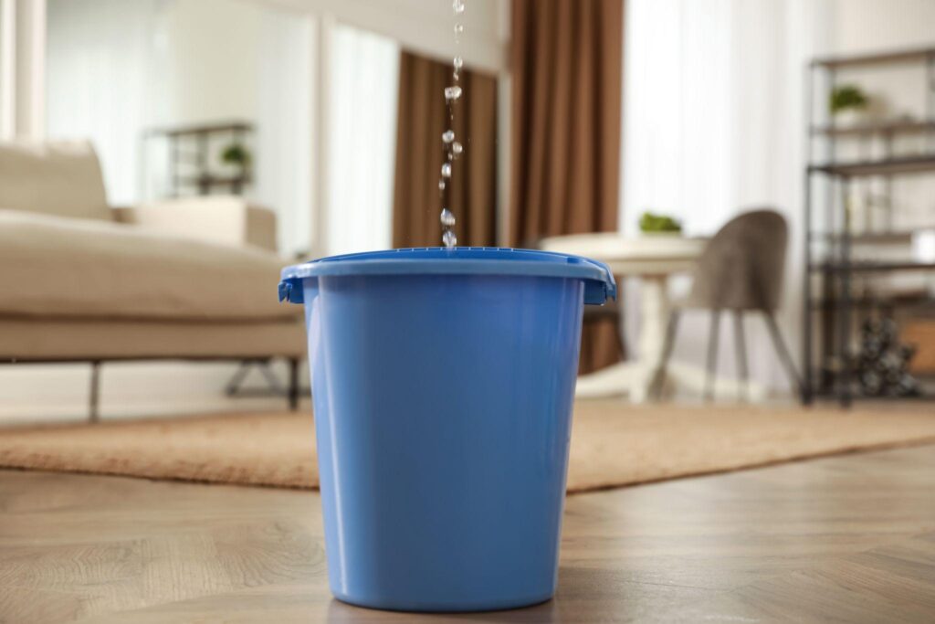 A blue trash can on the floor with water pouring out of it.