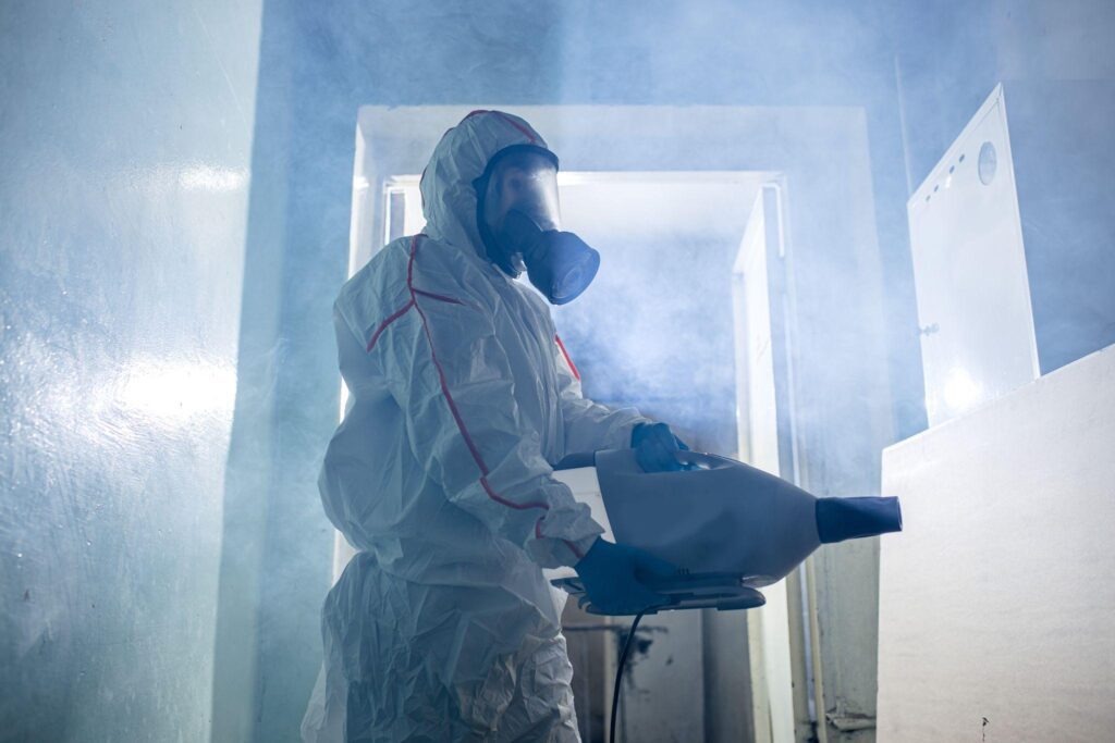 A person in white suit and mask spraying water.