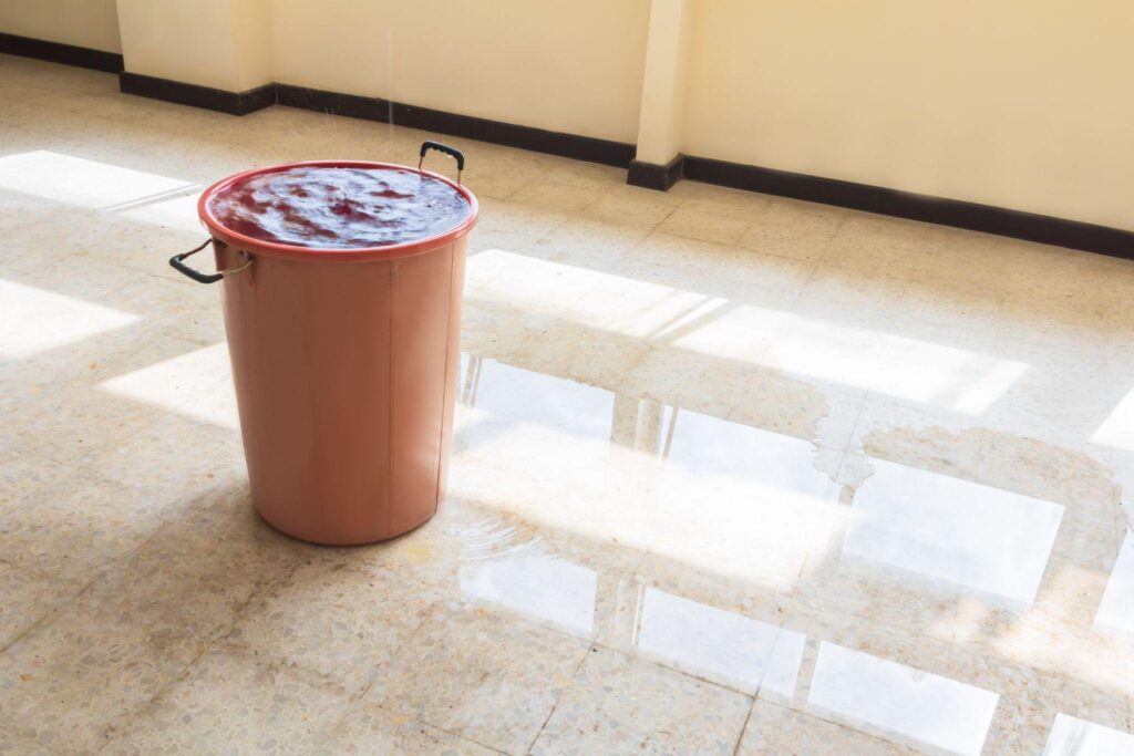 water leak drop interior office building in red bucket from Ceiling and flow on terrazzo floor
